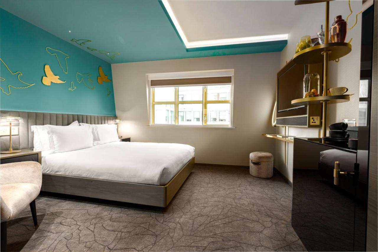 Middle Eight - Covent Garden - Preferred Hotels And Resorts Лондон Экстерьер фото The photo shows a modern hotel room featuring a large bed with white linens positioned against a wall. The decor includes a striking turquoise ceiling and decorative elements, such as yellow motifs, on the wall. There are large windows allowing natur