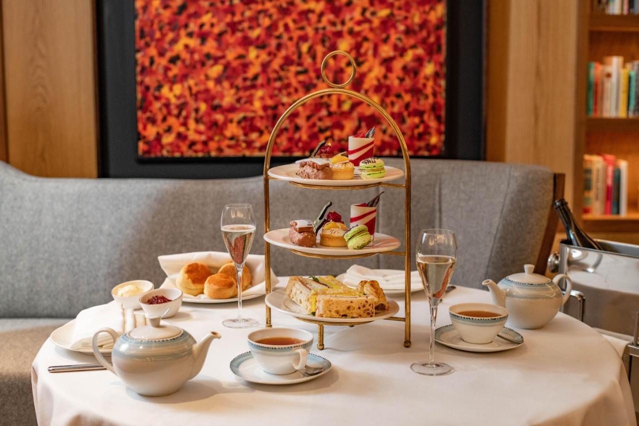 Middle Eight - Covent Garden - Preferred Hotels And Resorts Лондон Экстерьер фото The photo shows an elegant afternoon tea setup on a white tablecloth. At the center, there is a multi-tiered stand displaying a variety of pastries and desserts, including cakes and colorful sweets. Surrounding the stand are teapots and teacups, read
