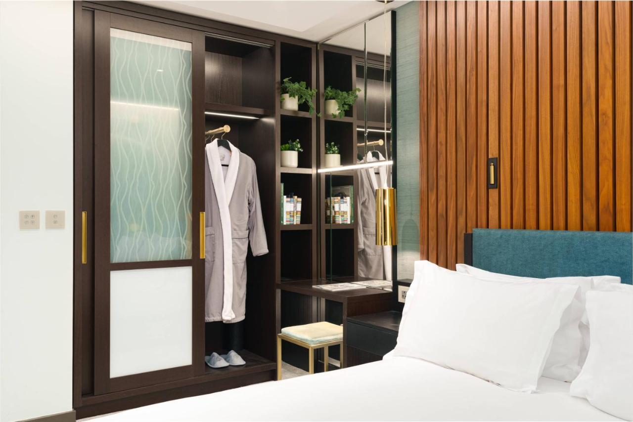 Middle Eight - Covent Garden - Preferred Hotels And Resorts Лондон Экстерьер фото The photo shows a cozy hotel room featuring a neatly made bed with white bedding. On the side, there is a wardrobe with sliding glass doors. Inside the wardrobe, a light-colored robe is hanging, and there are shelves with small plants and toiletries 