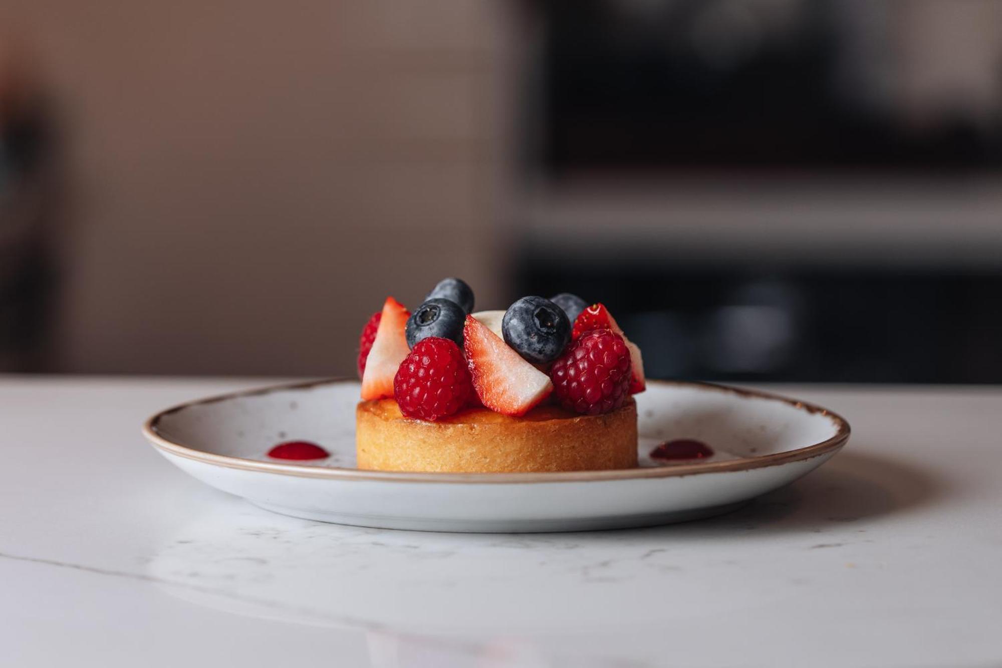 Middle Eight - Covent Garden - Preferred Hotels And Resorts Лондон Экстерьер фото The photo shows a delicious-looking dessert on a white plate. The dessert appears to be a small tart or cake topped with fresh strawberries, raspberries, and blueberries. It has a golden crust, and there are small dollops of a red sauce or fruit pure