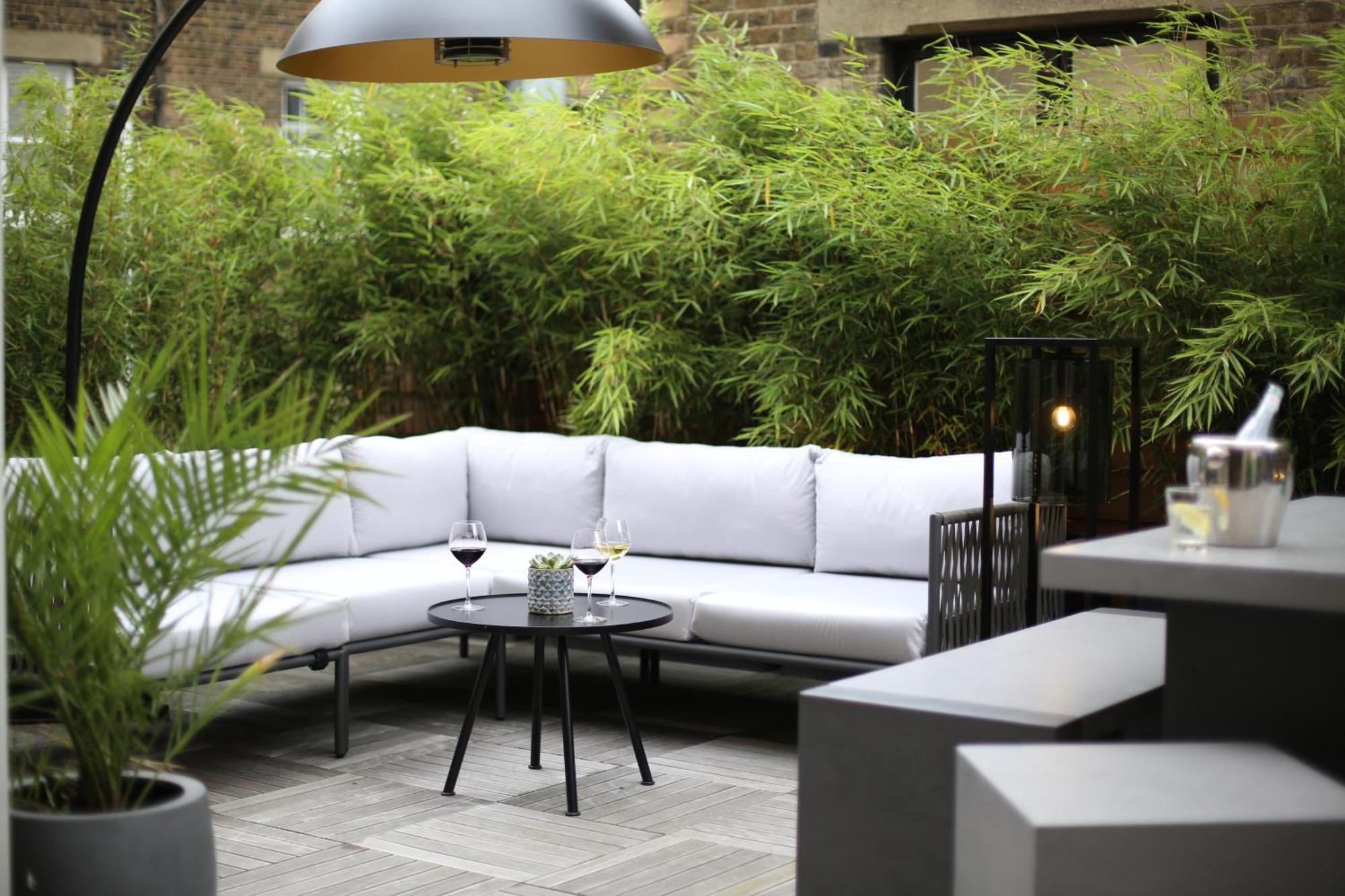 Middle Eight - Covent Garden - Preferred Hotels And Resorts Лондон Экстерьер фото The photo shows an outdoor seating area featuring a modern gray sectional sofa with plush cushions. In front of the sofa is a small, round black table with two glasses of wine on it, accompanied by a decorative plant or vase. Surrounding the area are